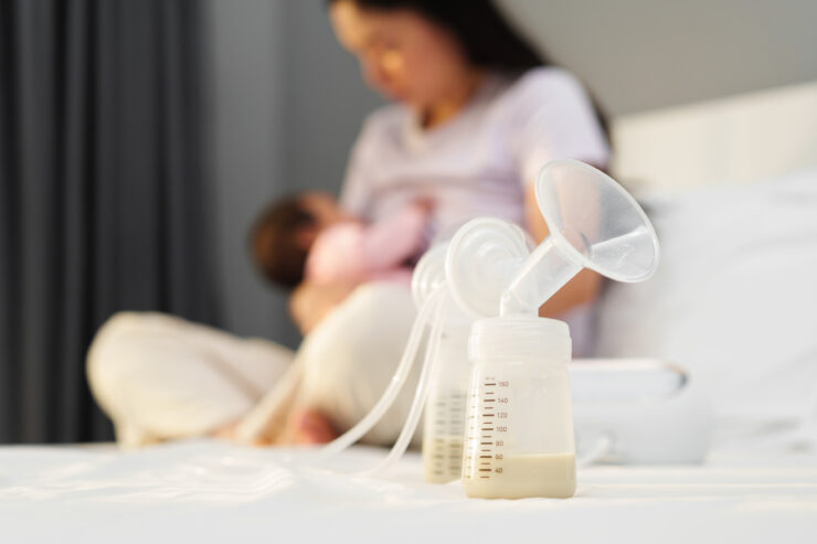 Afbeelding van twee flesjes gekolfde moedermelk en op de achtergrond een moeder die borstvoeding geeft.