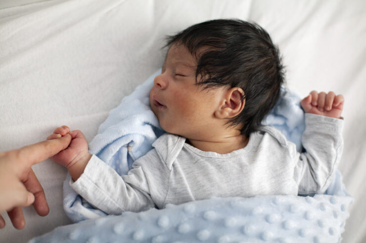 Slapende baby die de vinger van diens moeder vasthoudt.